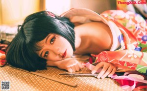 A woman in a colorful kimono sitting on a bed.