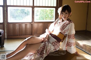 A naked asian woman sitting on a bed in front of a window.