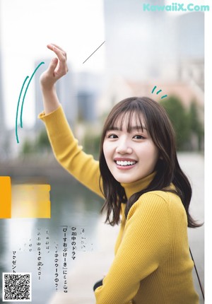 A woman in a yellow sweater and plaid skirt holding a camera.