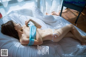 A woman in a white bikini sitting on a bed.