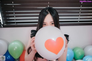 A woman sitting on a bed holding a bunch of balloons.
