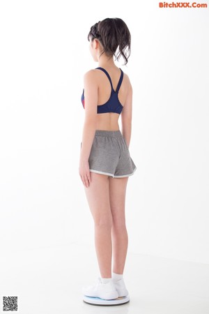 A woman in a blue top and gray shorts leaning against a wall.