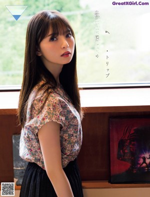 A woman in a blue shirt and striped shorts leaning against a wall.