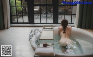 A naked woman sitting in a bathtub next to a window.