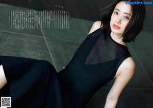 A woman in a black dress leaning against a wooden wall.