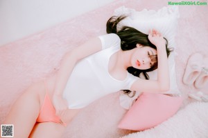 A woman in a white shirt and pink panties sitting on a bed.