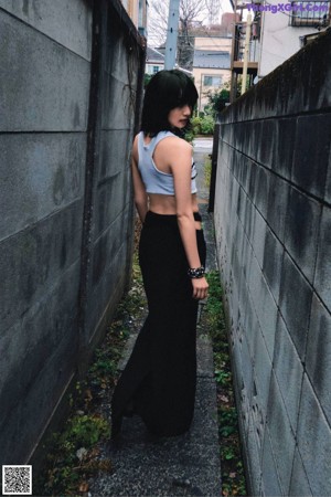 A woman leaning against a wall wearing a white top and black shorts.